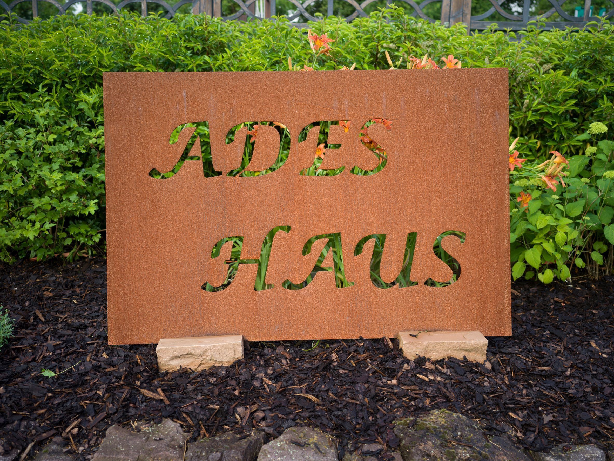 Uma placa com o texto 'ADES HAUS' em um jardim.