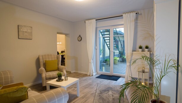 A living room with a sofa, armchair, coffee table, and a large window with curtains. - Guest / fitter room ADES HAUS - uncomfortable somewhere else! (Überherrn)