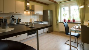 A modern kitchen with wooden beams, a built-in dishwasher, a coffee maker, and a dining area with a chair and table. - Guest / fitter room ADES HAUS - uncomfortable somewhere else! (Überherrn)