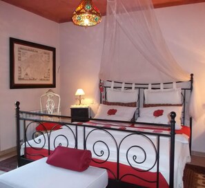 A bed with a metal frame, a canopy, and red and white bedding. There is a nightstand with a lamp and a framed map on the wall.