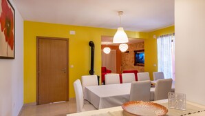 Un coin repas avec une table dressée pour quatre personnes, des chaises blanches, une porte en bois et un mur jaune.