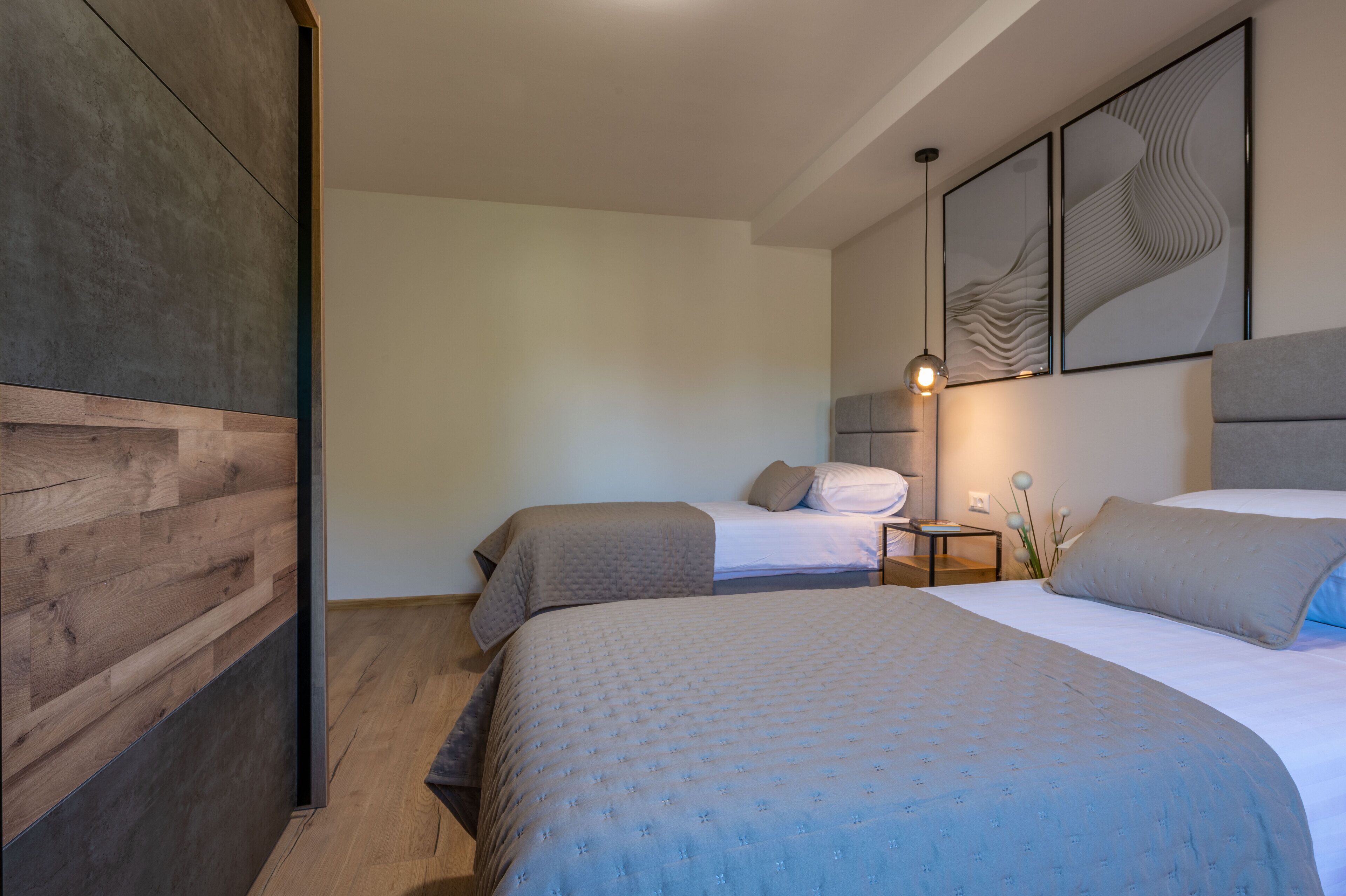 Ein modernes Schlafzimmer mit zwei Betten, einer Wand aus Holzvertäfelung und abstrakter Wandkunst.