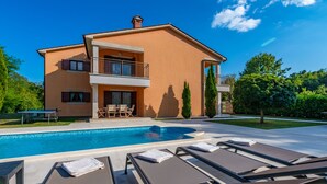 Une maison à deux étages dotée d’une piscine, de chaises longues et d’un espace patio.
