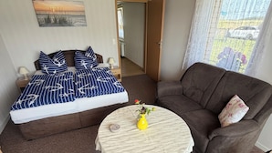A room with a bed, a sofa, a small table with a vase, and a window with curtains. - Comfortable, affordable, quiet, located at the harbor and surrounded by meadows, pets welcome (Pruchten)