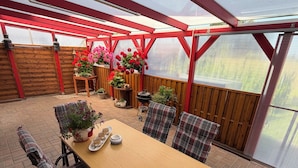 A covered patio with a wooden table and plaid chairs, surrounded by potted plants and a wooden fence. - Comfortable, affordable, quiet, located at the harbor and surrounded by meadows, pets welcome (Pruchten)