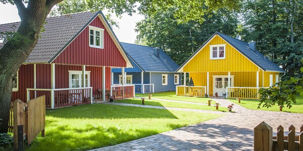 Une rangée de cabanes en bois aux couleurs vives, avec une cour verdoyante et un sentier en bois.