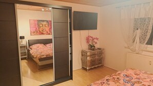 Quarto com cama, cômoda, televisão e janela com cortinas.