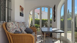 A sunlit room with a wicker sofa, a table, and a view of a building through arched glass doors. - T-4711, Villa Sol, villa with private pool, 600 m from the sea (Els Poblets)