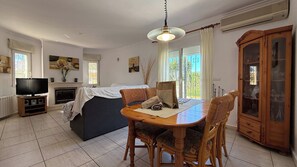 Ein gemütliches Wohnzimmer mit Fernseher, Kamin, Esstisch und Korbsesseln.