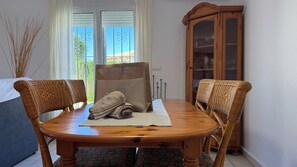 Een eetruimte met een houten tafel, rieten stoelen, een kast met glazen deuren en uitzicht door het raam.