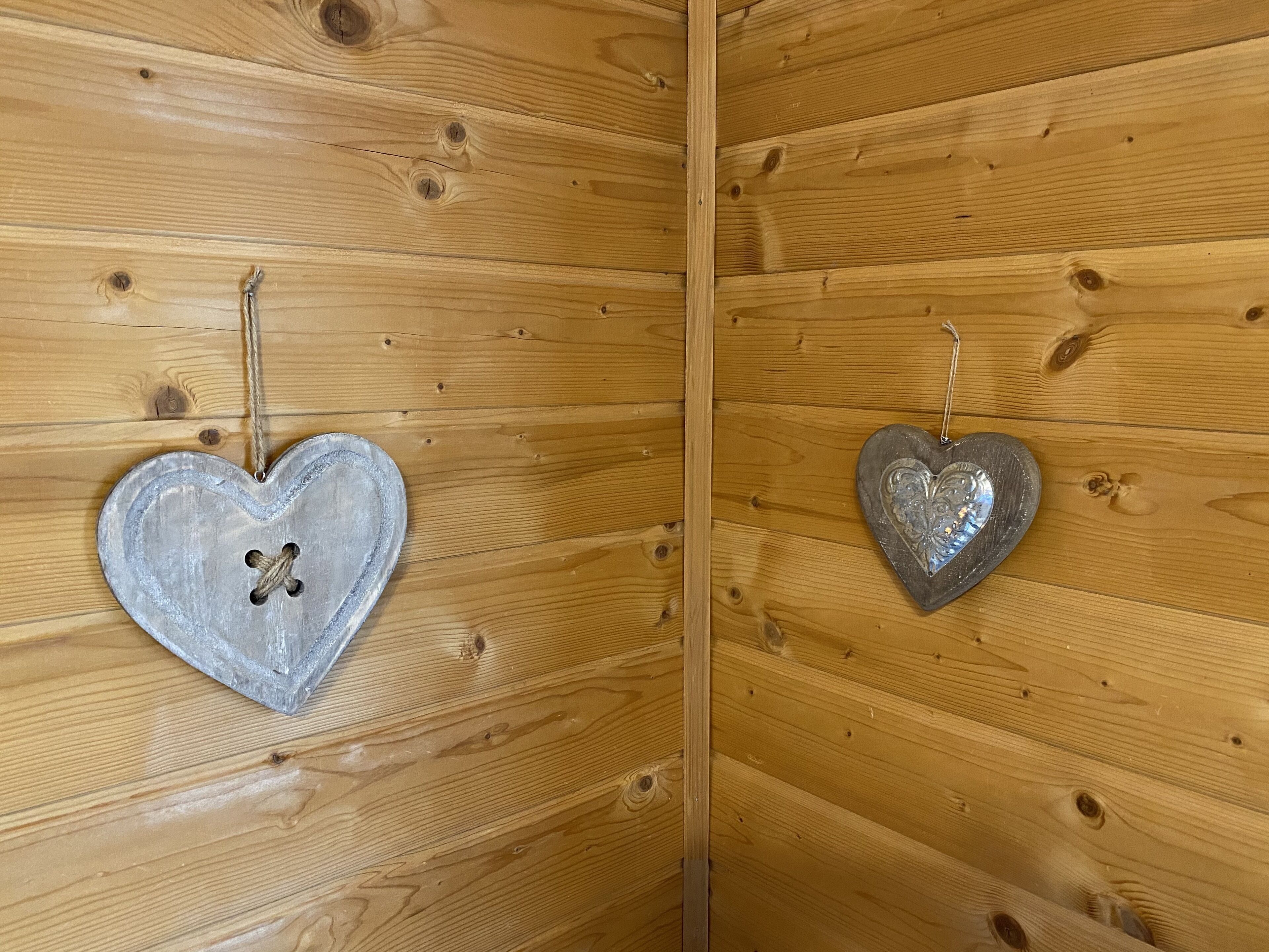 Two heart-shaped metal decorations hanging on a wooden wall.