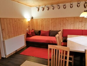 Une pièce chaleureuse avec des murs lambrissés, un canapé rouge, une table en bois et un luminaire fixé au mur.