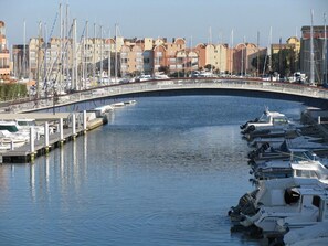 A marina with boats docked, a curved bridge, and buildings in the background.