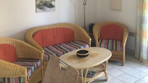 A room with wicker furniture, a round table with a bowl, a picture of the ocean, and a floor lamp. - Exclusively furnished apartment, 3 minutes from the beach (Gruissan)