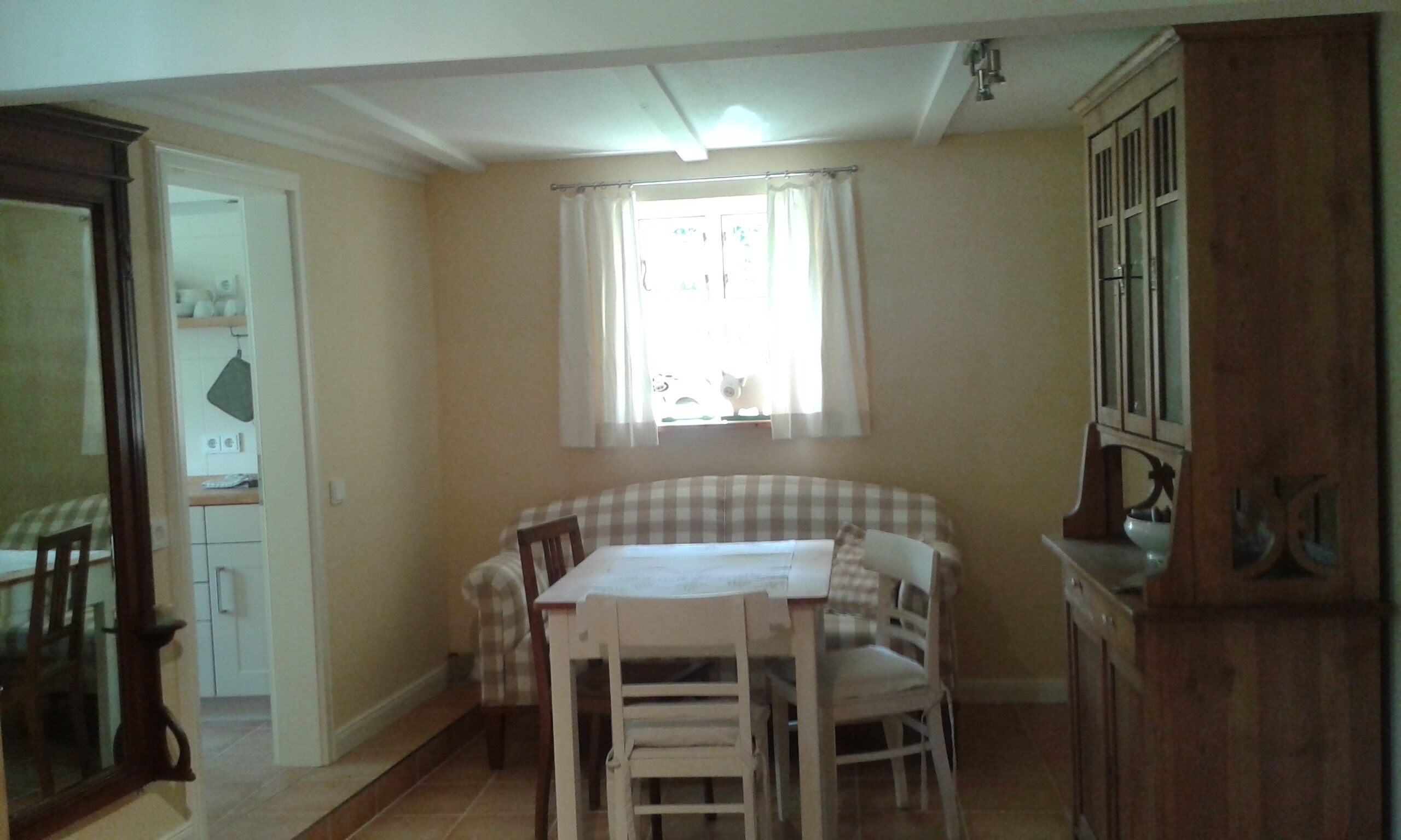 A dining area with a table and chairs, a window with curtains, and a kitchen area with cabinets and a sink.
