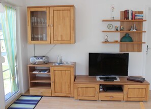 Ein Wohnzimmer mit Holzschrank, Fernseher, Bücherregalen und dekorativen Gegenständen sowie einem Radio.