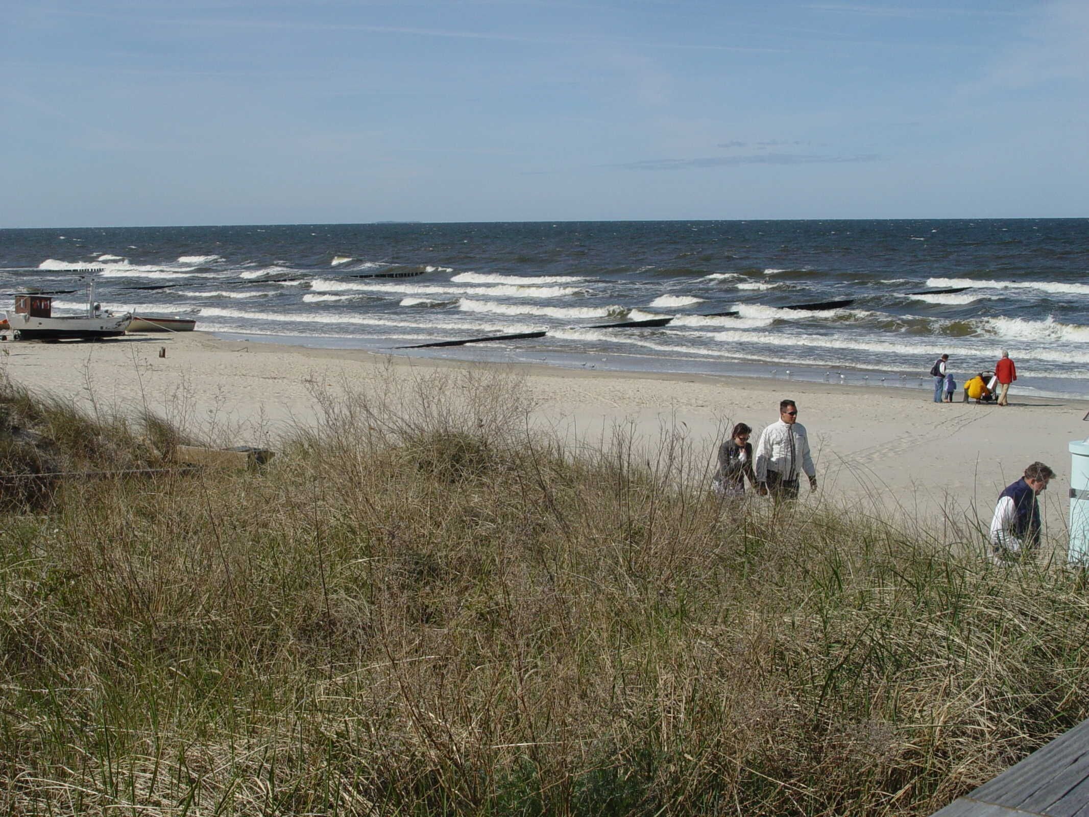 Ein Strand mit Wellen, einem Steg und Spaziergängern.