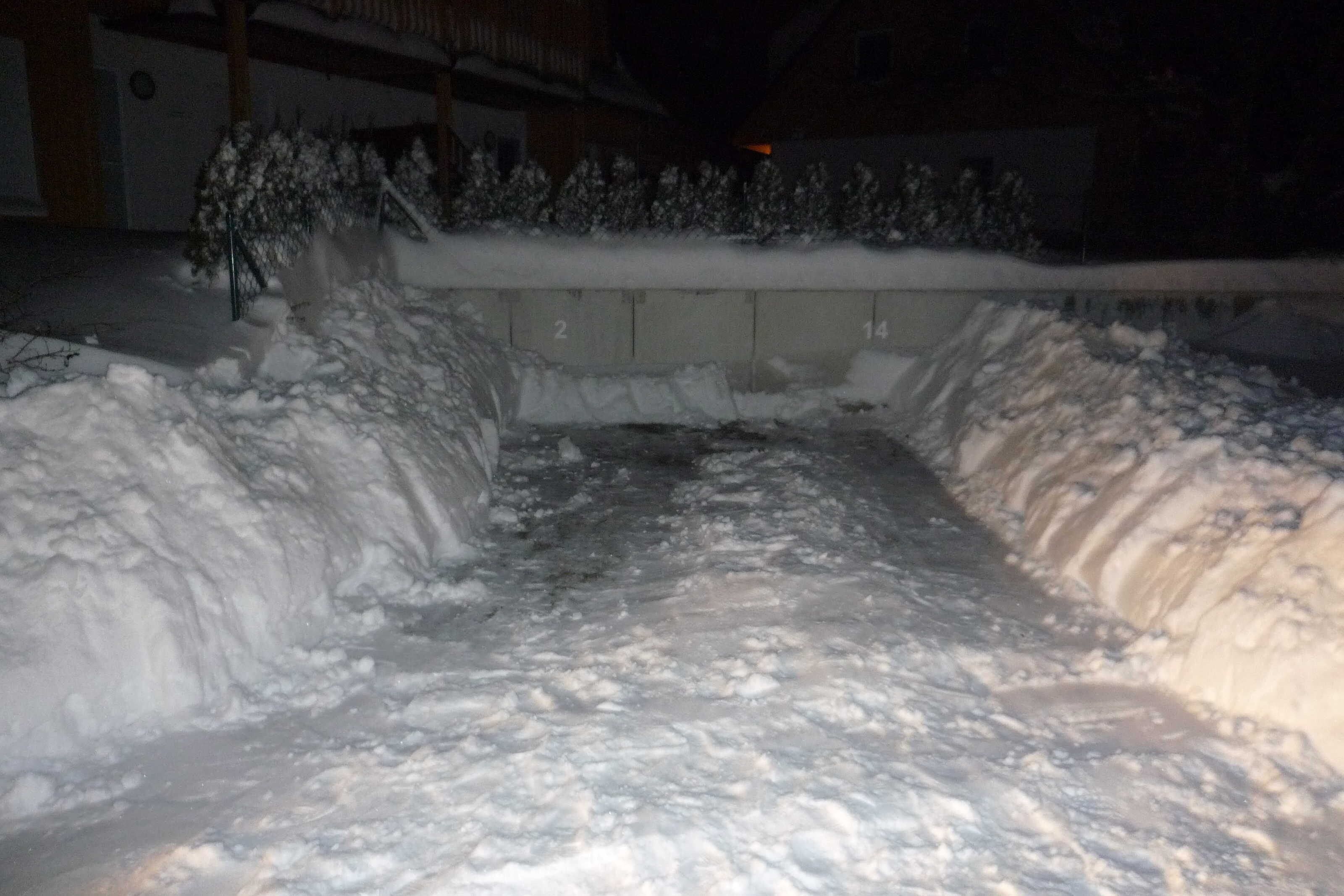 A snow-covered outdoor area with a concrete barrier, snowbanks, and a small water channel.