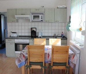 A kitchen with a microwave, coffee maker, toaster, and a dining table with chairs.