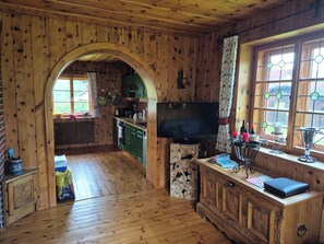 A wooden cabin interior with a kitchen, a television, and a window with curtains.
