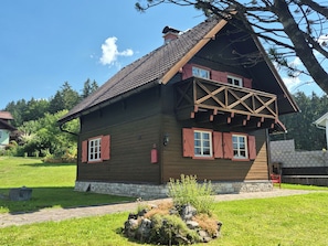 A wooden house with a stone foundation, a balcony, and a stone wall in the background.