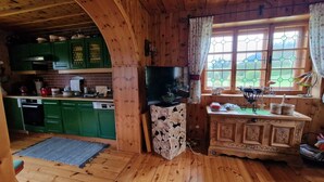 A rustic cabin interior with a wooden interior, a green kitchen with a built-in stove, a television on a wooden stand, and a window with a view of greenery. - cozy house in a sunny place with a fantastic mountain panorama (Bad Mitterndorf)