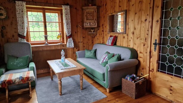 Una habitación acogedora estilo cabaña con un sofá verde, una mesa de madera, una silla y una ventana con cortinas.