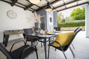 A dining area with a round table, black chairs, and a yellow cushion. There is a clock on the wall and a foosball table in the background.