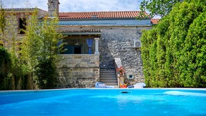 A stone building with a red-tiled roof, a swimming pool, and a staircase leading to a balcony.