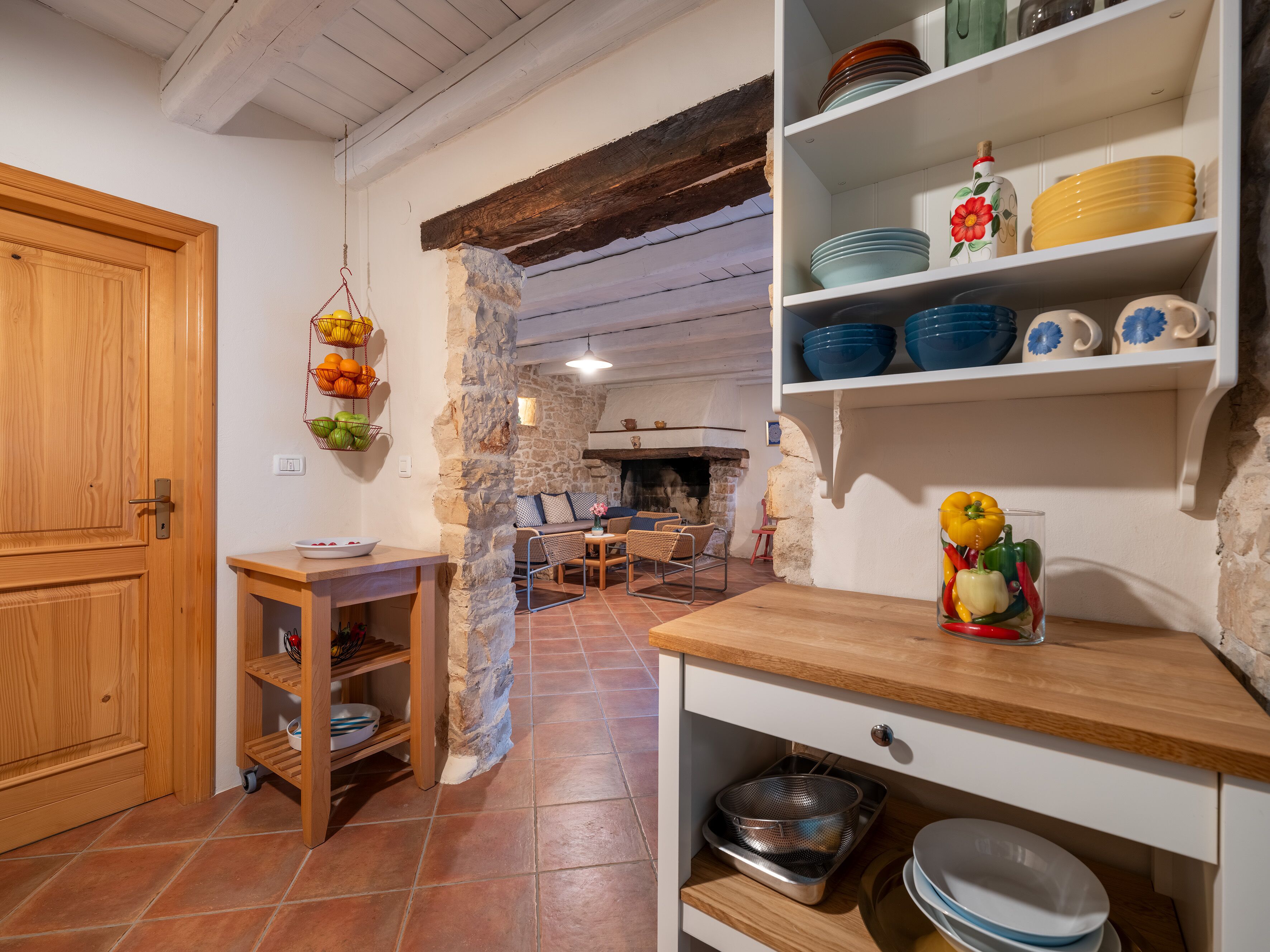 Una cocina rústica con pared de piedra, armarios de madera y suelo de baldosas.