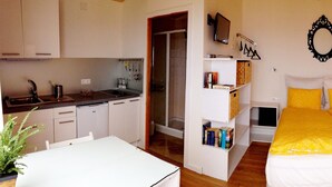 Een kleine kamer met een bed, een kitchenette en een badkamer.