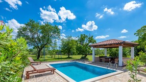 A swimming pool with lounge chairs and a pergola, surrounded by greenery and a clear sky. - Quiet and secluded, minutes to beach, private pool in a wonderful garden (Trget)