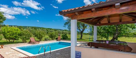 Une piscine avec des chaises longues, une pergola et une terrasse en pierre.