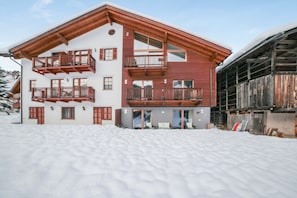 Un immeuble à plusieurs étages, doté de balcons, de grandes fenêtres et dont le sol est recouvert de neige.