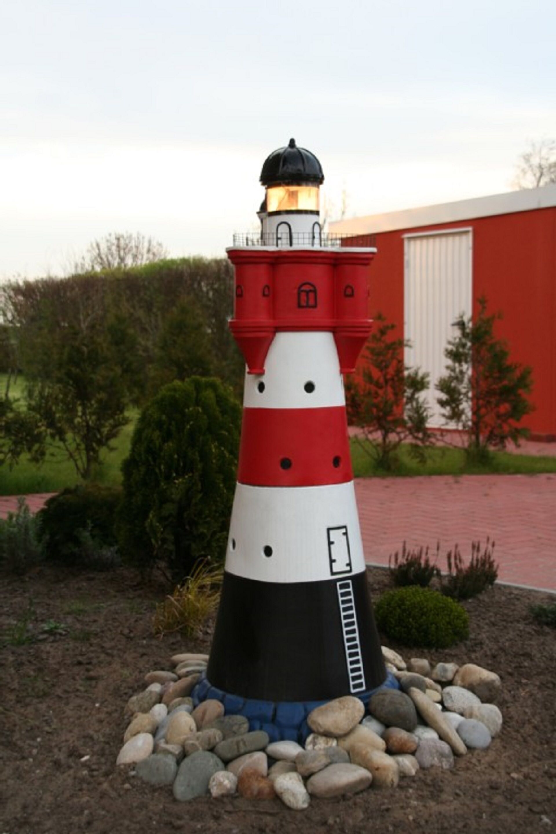 A lighthouse with a red and white striped pattern, surrounded by rocks and greenery.