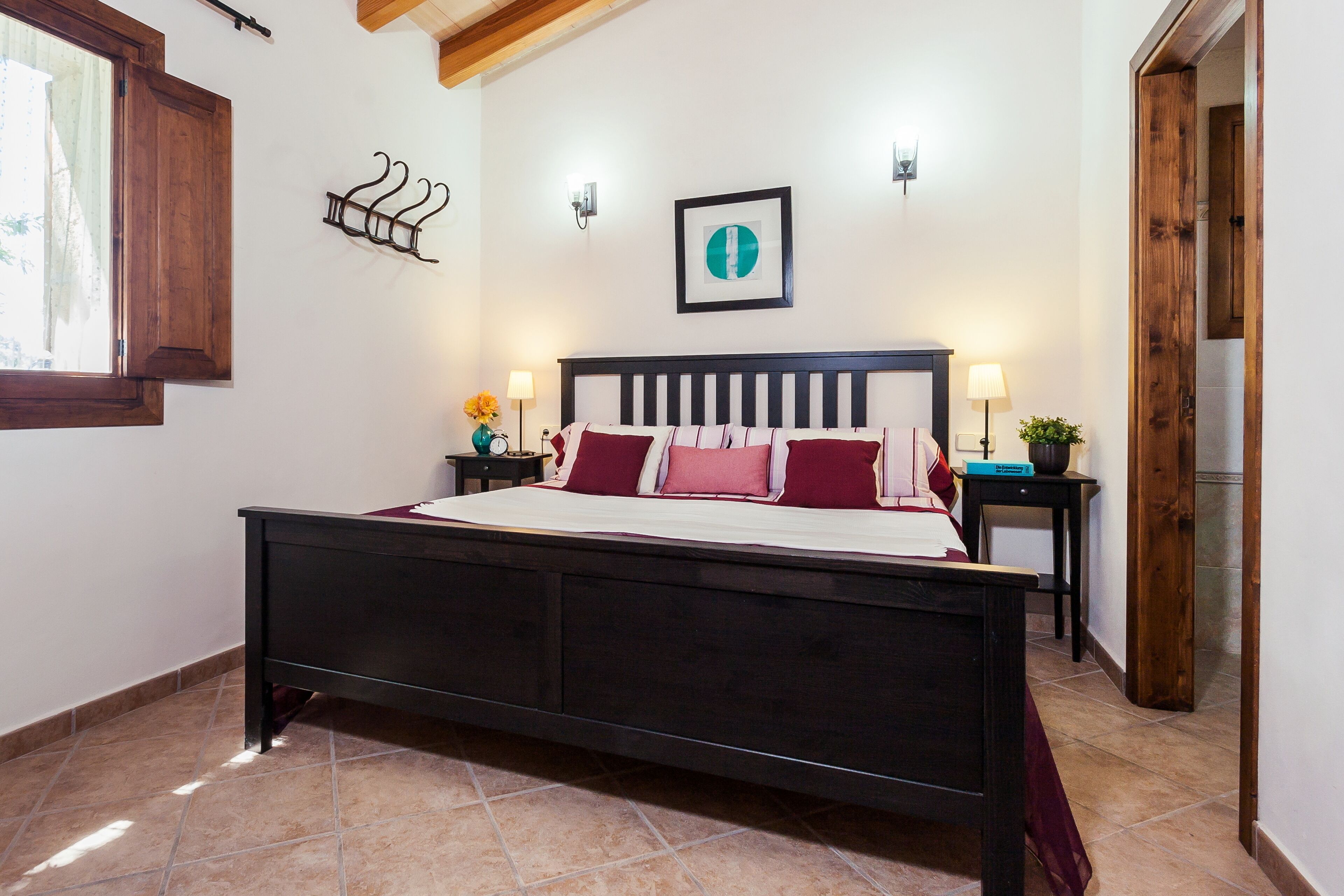 Une chambre à coucher avec un grand lit, deux tables de chevet, un luminaire fixé au mur et une fenêtre avec un cadre en bois.