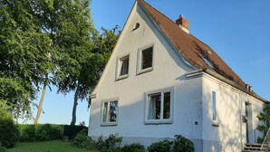 A white two-story house with a sloped roof, a chimney, and a small garden with a wooden bench and a gravel path. - Enjoy stunning views over Kiel and nature (Kiel)