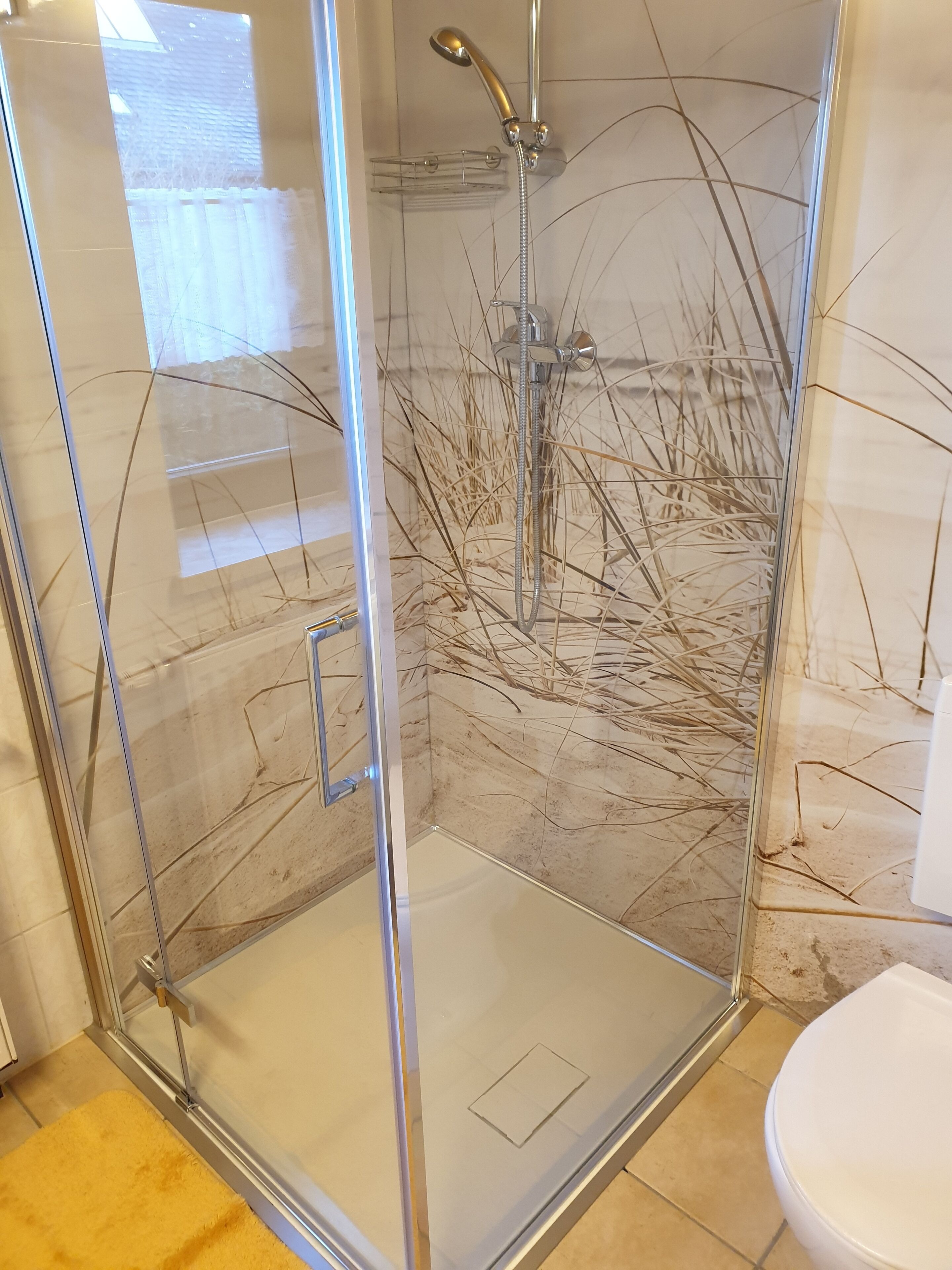 Une douche fermée par des parois en verre, dotée d’un pommeau de douche à main et d’un robinet mural.