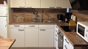 A modern kitchen with white cabinets, a wooden countertop, a stainless steel sink, a coffee maker, and a microwave. - Comfortable summer cottage in a beautiful surrounding (Marienberg)