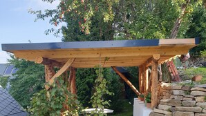 A wooden pergola structure with a stone wall and a hanging plant. - Comfortable summer cottage in a beautiful surrounding (Marienberg)