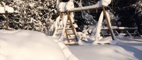 Een houten constructie bedekt met sneeuw, mogelijk een slede of speeltoestel, omringd door sneeuw en bomen.