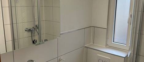 A modern bathroom with a white sink, a toilet, a glass shower enclosure, and a window.