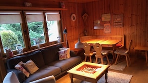 A cozy cabin interior with a wooden interior, a sofa, a dining table with chairs, and a window with a view of greenery. - Pure nature - detached, quietly situated vacation home for 4 people (Feldberg)