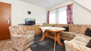 Ein Wohnzimmer mit einer Couch, Sesseln, einem Holztisch und einem Fernseher.