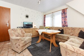 A living room with a sofa, armchairs, a wooden table, and a television. - Apartment small - Ferienhaus Zur Schmiede (Dunum)
