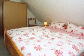 A bedroom with a wooden bed, floral bedding, a nightstand with a lamp, and a wardrobe.