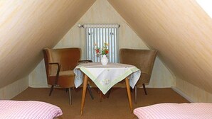 Ein gemütliches Schlafzimmer im Dachgeschoss mit zwei Einzelbetten, einem kleinen Tisch mit Blumenvase und einem Sessel.