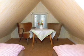 Un dormitorio acogedor en el ático con dos camas individuales, una mesita con un jarrón de flores y una silla.