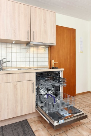 Une cuisine avec des meubles de rangement en bois, un lave-vaisselle encastré et un évier en acier inoxydable.