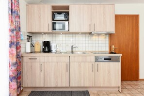 Una cocina con armarios de madera, microondas, tostadora, pileta y lavavajillas.